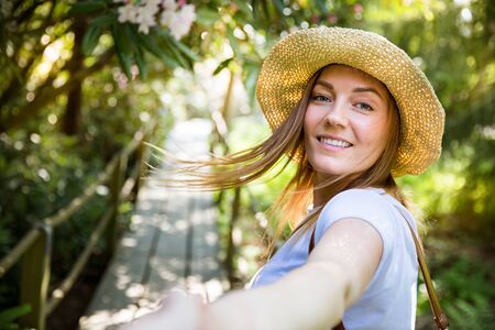 Beautiful woman in straw hat travel in tropic forest, walking along wooden path, leading her partner.の写真素材