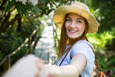 Beautiful woman in straw hat travel in tropic forest, walking along wooden path, leading her partner.の写真素材
