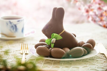 Beautiful served small table with Easter decorations on outdoor terrace. Little chocolate bunny with...