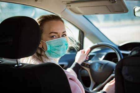 Woman in protective mask driving a car on road. Safe traveling.の写真素材