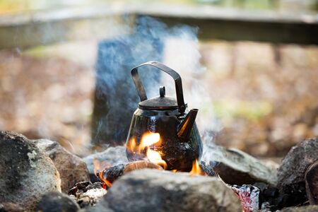 Man and woman making coffee in big kettle on campfire in forest on shore of lake, making a fire, grilling. Happy couple exploring Finland. Scandinavian landscape.の写真素材