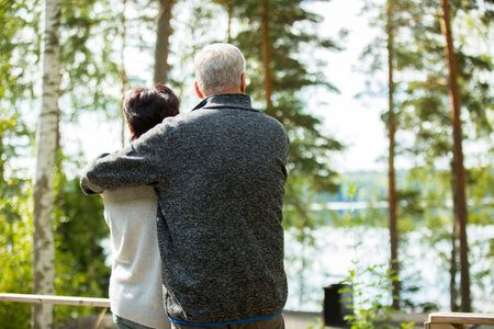 Rear view of senior couple standing in the park and looking at the lakeの写真素材