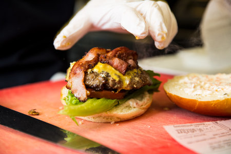 Preparing delicious burgers. Chef cooking meat burgers with bacon, cheese and vegetables. Close-up.の写真素材
