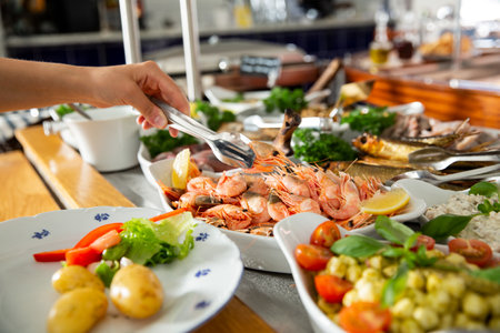 A restaurant customer puts delicious shrimp on a plate. Seafood buffet lunch in a cafeの写真素材