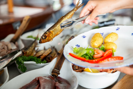 A restaurant customer puts delicious smoked Baltic herring on a plate. Seafood buffet lunch in a cafe in Finlandの写真素材