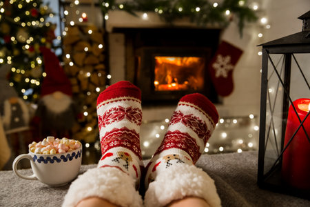 Couple enjoying by warm fireplace and warming up their feet in woolen socks with Christmas ornaments and Christmas tree and decorations background. Cozy Winter, Christmas and Family.の写真素材