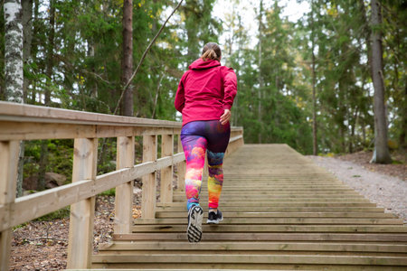 Athletic middle-aged woman running up the Fitness Stairs in a natural park in the woodsの写真素材