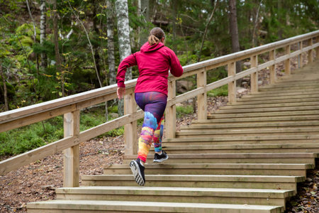 Athletic middle-aged woman running up the Fitness Stairs in a natural park in the woodsの写真素材