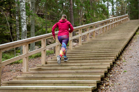 Athletic middle-aged woman running up the Fitness Stairs in a natural park in the woodsの写真素材