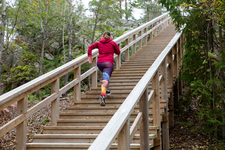 Athletic middle-aged woman running up the Fitness Stairs in a natural park in the woodsの写真素材