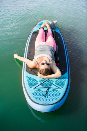 A young attractive woman lying on a SUP board, relaxing and smiling.