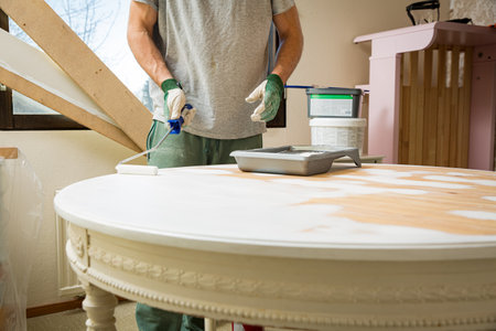 Middle-age man painting old wooden table with paint roller in white color. Furniture restoration, DIY repair, repair by oneself and home improvement. Recycling and sustainable lifestyleの写真素材