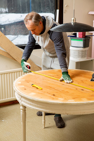 Middle-age man upcycling old wooden table using electric sander. Furniture restoration, DIY repair, repair by oneself and home improvement. Recycling and sustainable lifestyleの写真素材