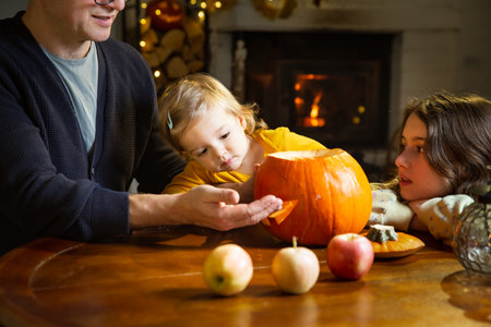 Father his toddler and daughter carving pumpkin jack o lantern, Halloween celebration at home. Fun craft and decoration at home. Happy children and their dad preparing for the holiday, decorating the house for Halloween partyの写真素材