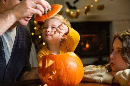 Father his toddler and daughter carving pumpkin jack o lantern, Halloween celebration at home. Fun craft and decoration at home. Happy children and their dad preparing for the holiday, decorating the house for Halloween partyの写真素材