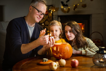 Father his toddler and daughter carving pumpkin jack o lantern, Halloween celebration at home. Fun craft and decoration at home. Happy children and their dad preparing for the holiday, decorating the house for Halloween partyの写真素材