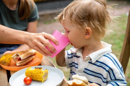 Mother spending quality time with children in backyard, sitting at a table. She is pouring water into glasses on a sunny day. Family outdoor lifestyleの写真素材