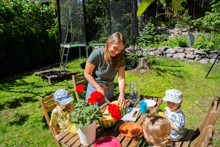 Mother cutting watermelon with toddlers at a backyard table. Sunny summer day, family time, and cozy...