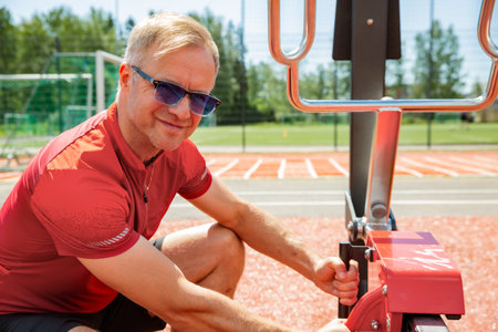 Middle-aged man adjusting weights on outdoor gym equipment during a summer workout. Focused training in natural environment.の写真素材