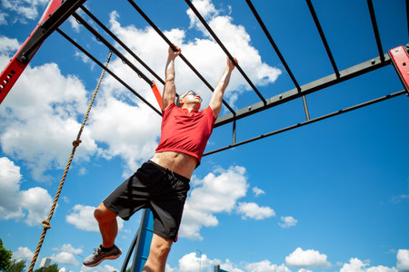 Active 50-year-old man uses monkey bars at an outdoor fitness station, training grip and upper body...