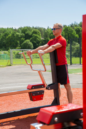 Active middle-aged man working out at an outdoor fitness park on a sunny summer day. Horizontal row gym equipment, Upper and middle back and bicepsの写真素材