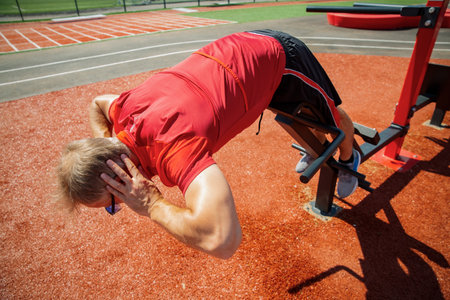 Middle-aged man working out on an adjustable back extension bench. Strengthens back extensors. Outdoor training supports mobility and fitness.の写真素材