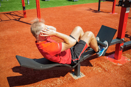 Man training on an adjustable abdominal bench. Targets core and abs. Outdoor workout improves core...