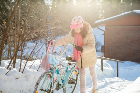 Tween walking home with her bicycle on a sunny winter day in a Finnish suburb. Snow on the ground, real moment of everyday Nordic life.の写真素材