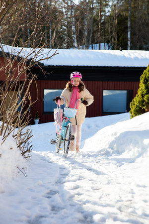 Tween walking home with her bicycle on a sunny winter day in a Finnish suburb. Snow on the ground, real moment of everyday Nordic life.の写真素材