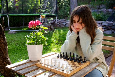 Father and tween daughter playing chess in their backyard on a summer day. Quality family time and mental development in a relaxed outdoor setting.の写真素材