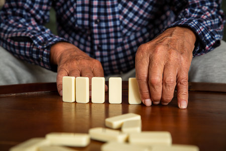 Close-up of elderly fathers hands placing dominoes on the table during a quiet game with his adult...