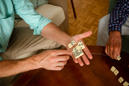Close-up of adult son and elderly fathers hands as they play dominoes together at home, highlighting connection, focus, and quiet bonding time.の写真素材