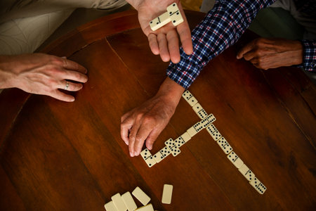Close-up of adult son and elderly fathers hands as they play dominoes together at home, highlighting connection, focus, and quiet bonding time.の写真素材