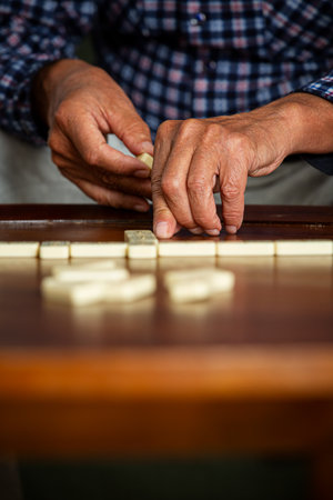 Close-up of adult son and elderly fathers hands as they play dominoes together at home, highlighting connection, focus, and quiet bonding time.の写真素材