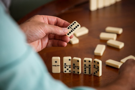 Close-up of adult son and elderly fathers hands as they play dominoes together at home, highlighting connection, focus, and quiet bonding time.の写真素材