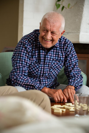 Elderly man shuffles domino tiles before a game. A warm family tradition captured in a timeless,...