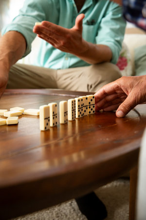 Close-up of adult son and elderly fathers hands as they play dominoes together at home, highlighting...