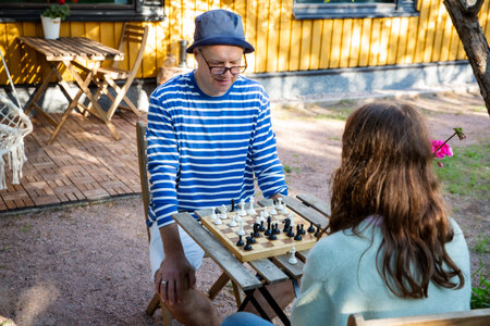 Father and tween daughter playing chess in their backyard on a summer day. Quality family time and...