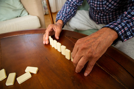 Close-up of elderly fathers hands placing dominoes on the table during a quiet game with his adult son - a tender moment of age and connection.の写真素材