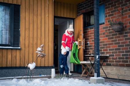 Grandmother with toddler heading outdoors in winter snow, dressed warmly with sled, enjoying family lifestyle and seasonal joy.の写真素材