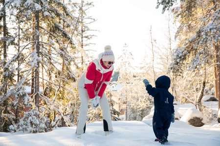 Healthy grandmother and toddler play in snowy forest, tossing snow, enjoying golden winter light,...