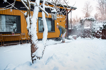 Man shoveling snow in backyard on a wintry morning, bundled in warm gear, highlighting everyday outdoor routine and seasonal lifestyle.の写真素材