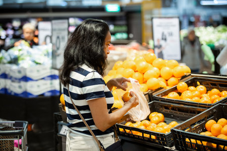 A middle-aged Filipina shopping for fresh mandarins in a supermarket, symbolizing healthy eating,...