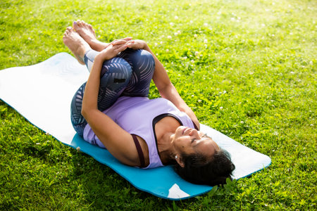 Middle aged woman of color practicing yoga on mat in park, embracing wellness, diversity, and balance in active modern lifestyle outdoors.の写真素材