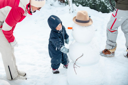 Grandmother and toddler building a snowman in snowy backyard. Joyful winter day, family bonding,...