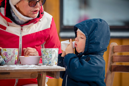 Child with cold symptoms outdoors in winter, wiping nose and coughing, seasonal flu, illness prevention, authentic family lifestyle.の写真素材