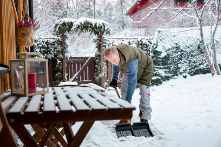 Man shoveling snow in backyard on a wintry morning, bundled in warm gear, highlighting everyday outdoor routine and seasonal lifestyle.の写真素材