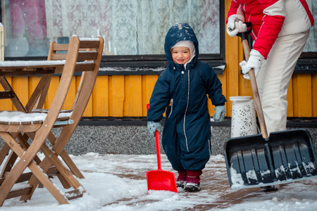 Elderly grandmother and toddler shoveling snow together in backyard, winter family bonding, outdoor activity, healthy seasonal lifestyle.の写真素材