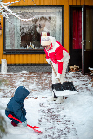 Elderly grandmother and toddler shoveling snow together in backyard, winter family bonding, outdoor activity, healthy seasonal lifestyle.の写真素材