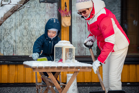 Elderly grandmother and toddler shoveling snow together in backyard, winter family bonding, outdoor activity, healthy seasonal lifestyle.の写真素材